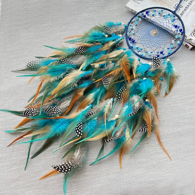 Un capteur de rêves en plumes bleu-vert et orange avec des motifs à pois, suspendu sur un fond gris clair.