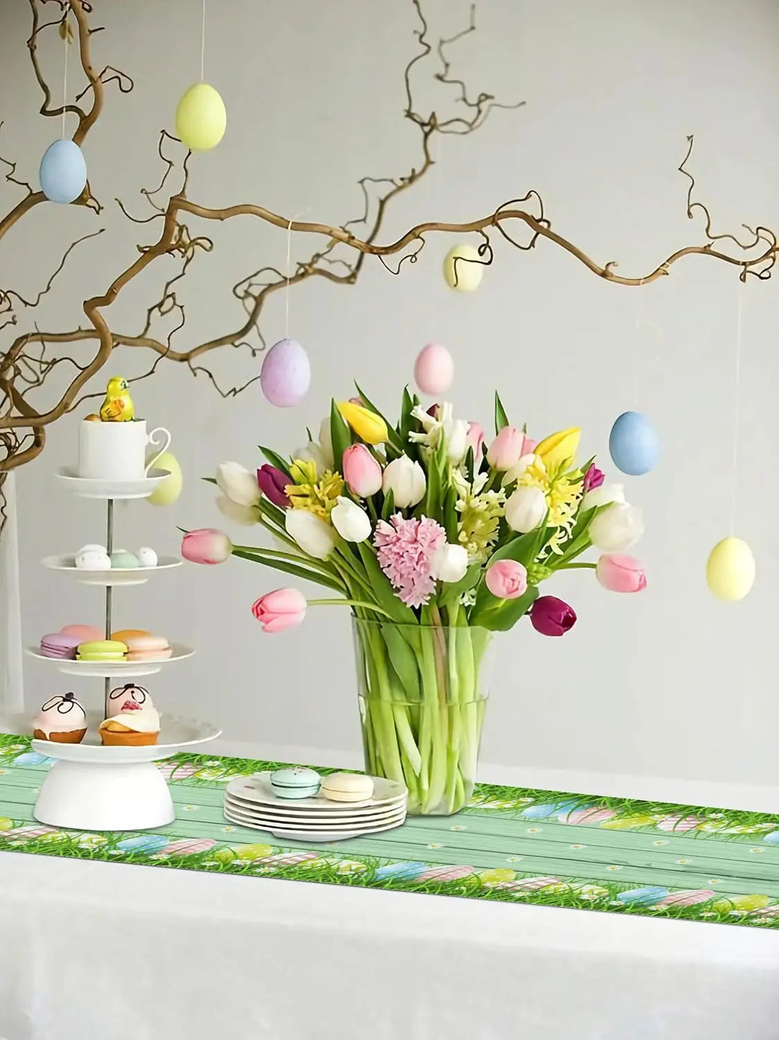 Bouquet printanier coloré de tulipes, oeillets et autres fleurs de saison sur un présentoir décoratif aux couleurs pastel, avec des macarons et des décorations de Pâques.