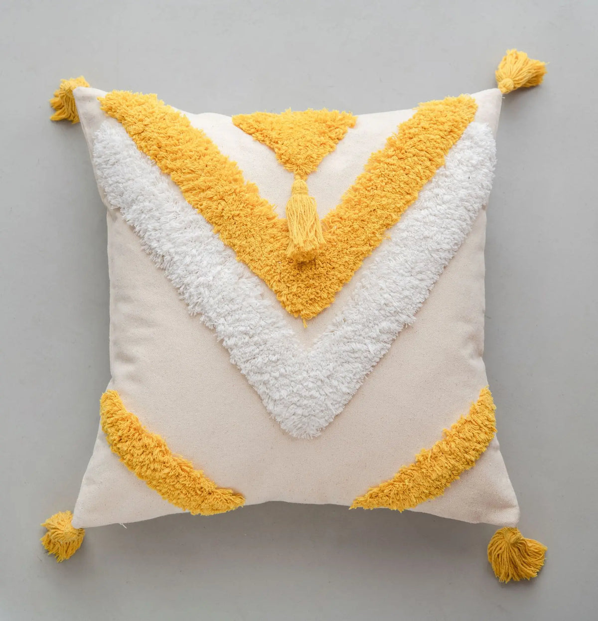 Coussin décoratif moelleux en tissu blanc avec des triangles géométriques jaunes et des pompons assortis.