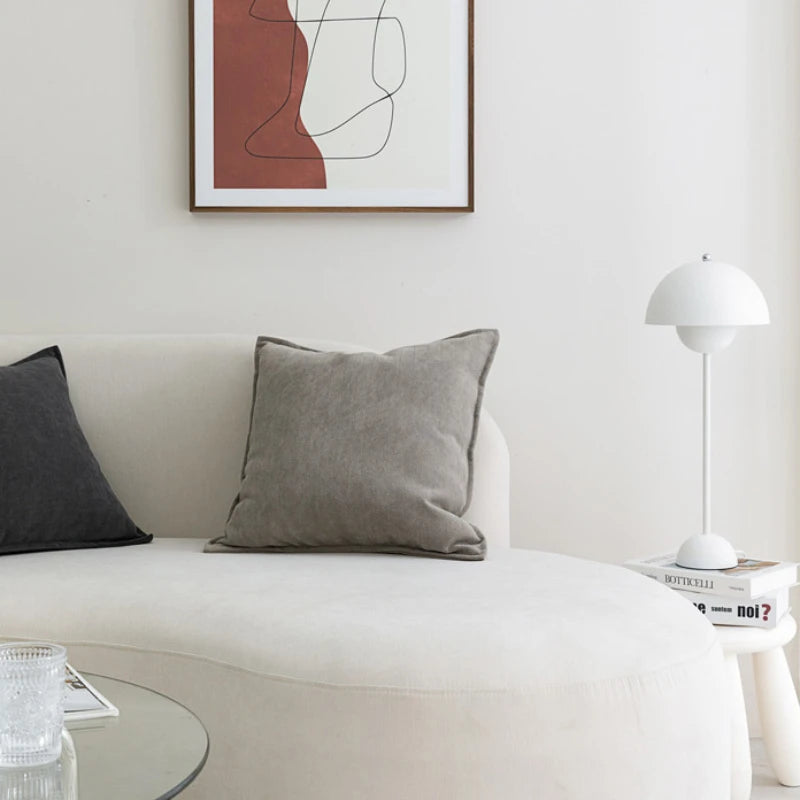 Salon élégant avec canapé blanc, coussins gris et lampe de table blanche, complété par une œuvre d'art abstraite au mur.