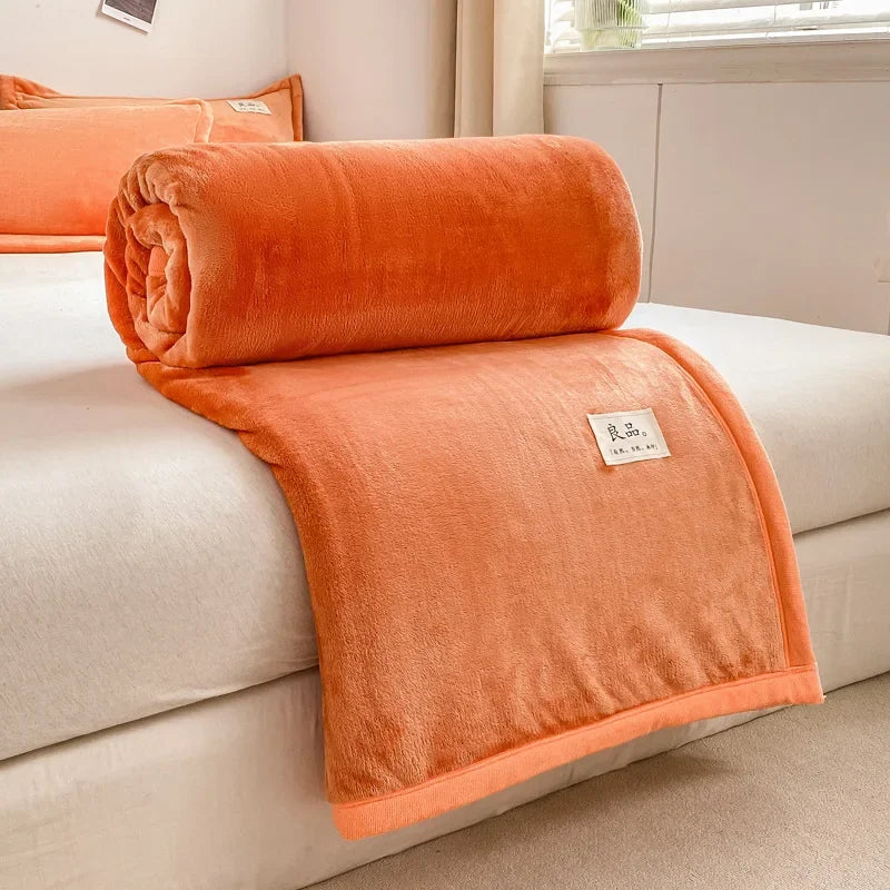 Une couverture moelleuse et confortable, dans une couleur orange lumineuse, reposant sur un canapé blanc dans un intérieur cosy.