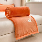 Une couverture moelleuse et confortable, dans une couleur orange lumineuse, reposant sur un canapé blanc dans un intérieur cosy.