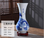 Vase en porcelaine blanche et bleue décoré de motifs de paysage, posé sur un support en bois.