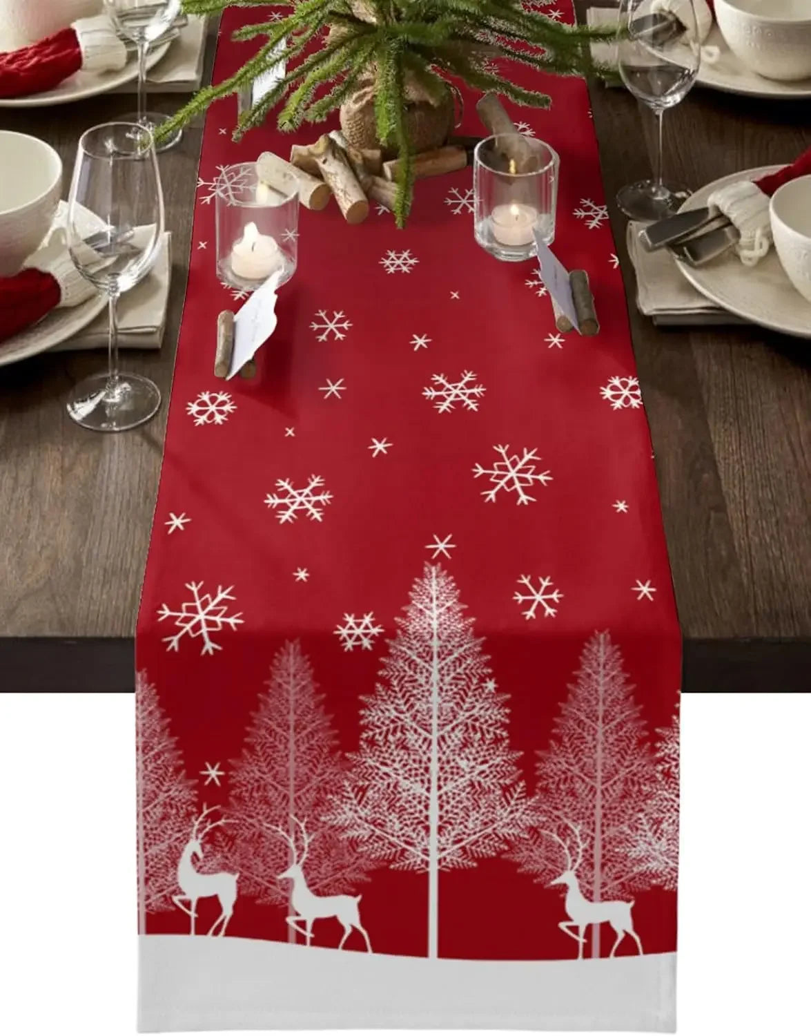 Chemin de table de Noël rouge avec motifs d'arbres et de cerfs enneigés, accompagné de bougies et d'éléments de décoration hivernale.
