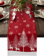 Chemin de table de Noël rouge avec motifs d'arbres et de cerfs enneigés, accompagné de bougies et d'éléments de décoration hivernale.