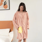 Une jeune femme porte un peignoir rose douillet et confortable dans une chambre avec un cadre décoratif au mur.