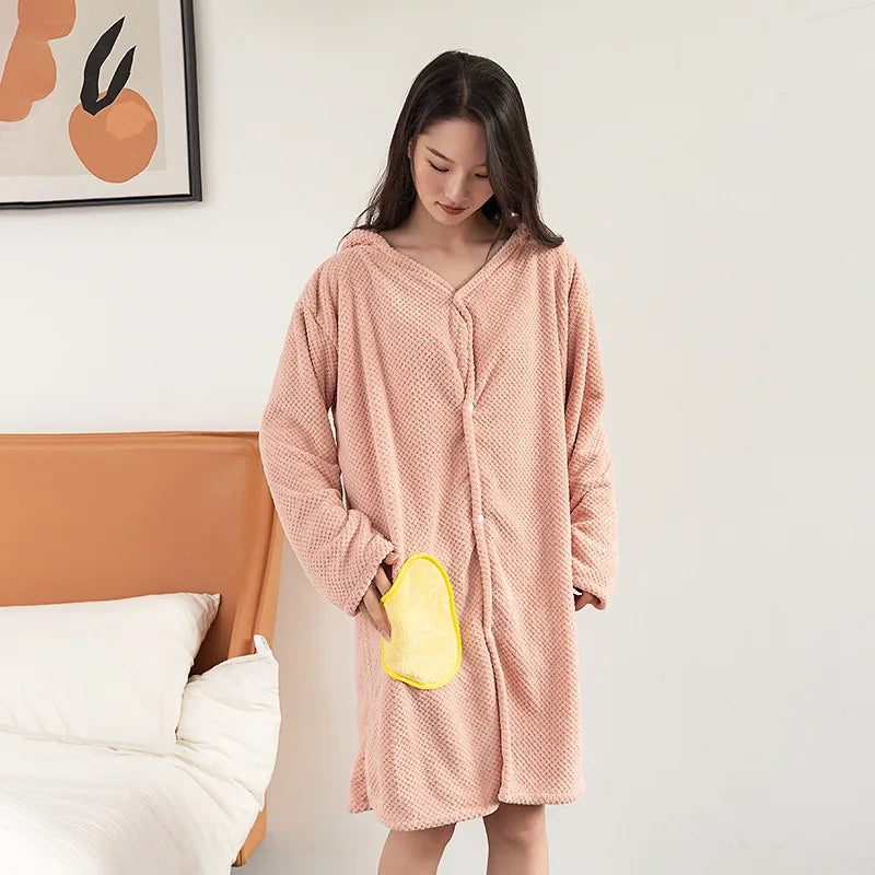 Une jeune femme porte un peignoir rose douillet et confortable dans une chambre avec un cadre décoratif au mur.