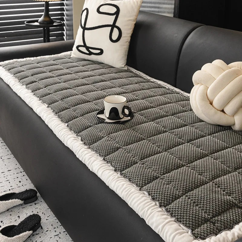 Une couverture en tricot grise et blanche sur un canapé noir, ornée de coussins décoratifs avec des motifs graphiques, crée une ambiance élégante et confortable dans ce salon.