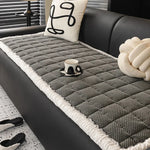 Une couverture en tricot grise et blanche sur un canapé noir, ornée de coussins décoratifs avec des motifs graphiques, crée une ambiance élégante et confortable dans ce salon.