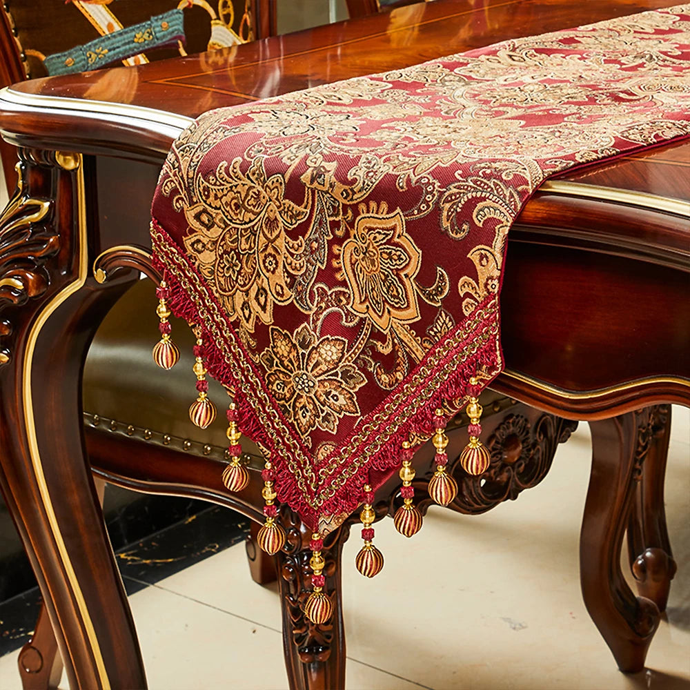 Élégant chemin de table en velours rouge décoré d'un motif floral doré, orné de perles pendantes en métal.