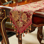 Élégant chemin de table en velours rouge décoré d'un motif floral doré, orné de perles pendantes en métal.