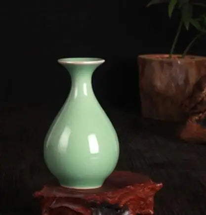 Un vase en porcelaine de couleur verte pastel, posé sur une surface en bois foncé avec des décorations florales.