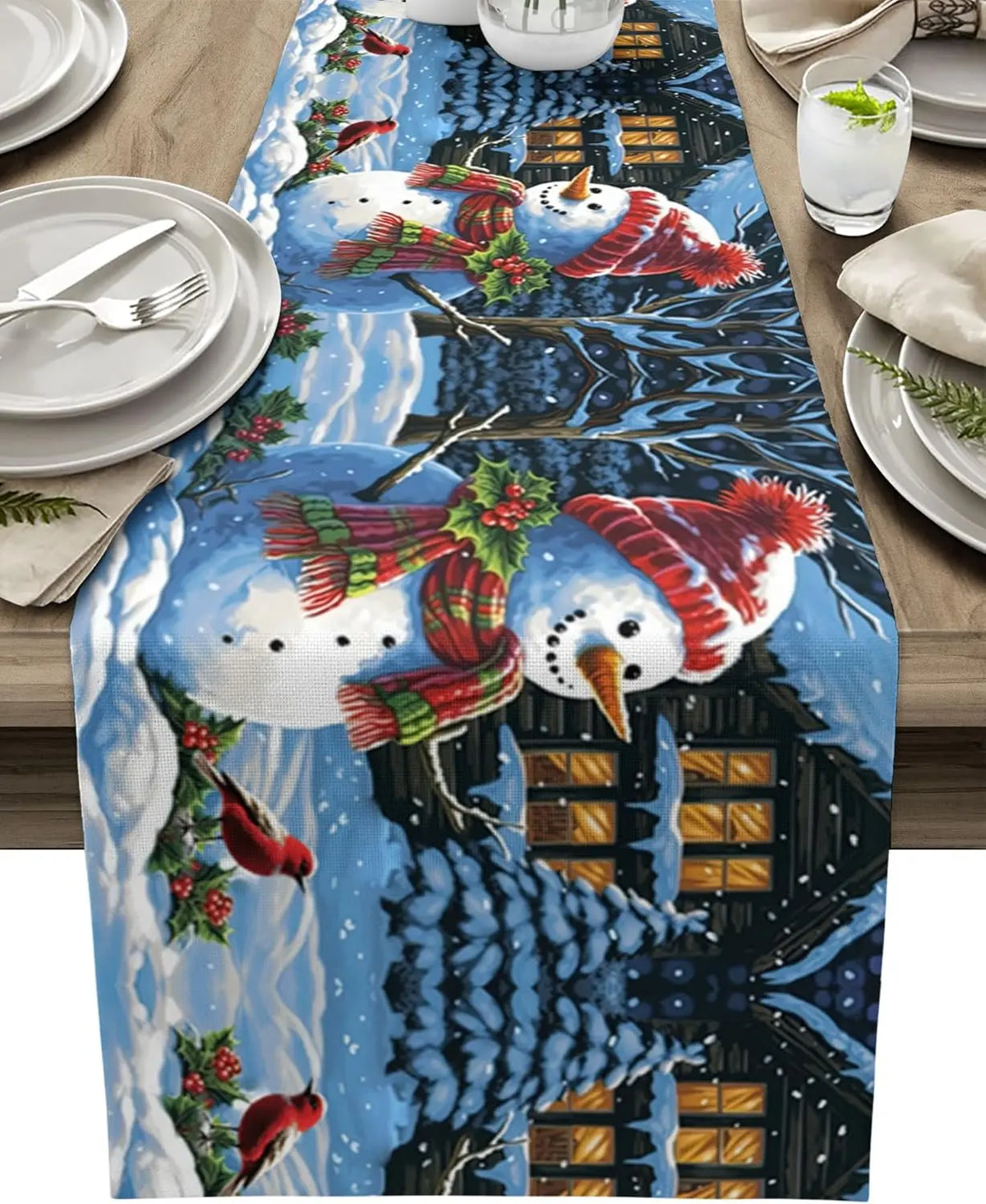 Deux bonhommes de neige vêtus de foulards rouges et verts se tiennent devant une maison enneigée dans un paysage hivernal animé de motifs de houx et de poissons rouges.