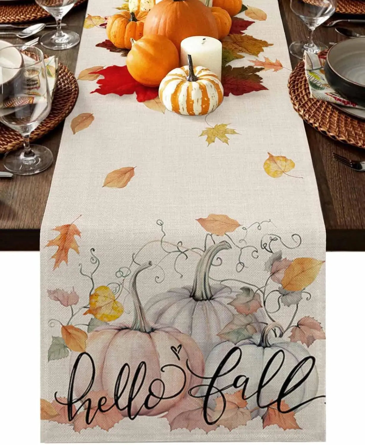 Une décoration de table automnale avec des citrouilles, des feuilles d'automne et une nappe ornée d'un motif d'automne avec l'inscription "Hello Fall".