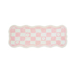 Tapis de salle de bain en forme ondulée avec motif de carrés roses et blancs.