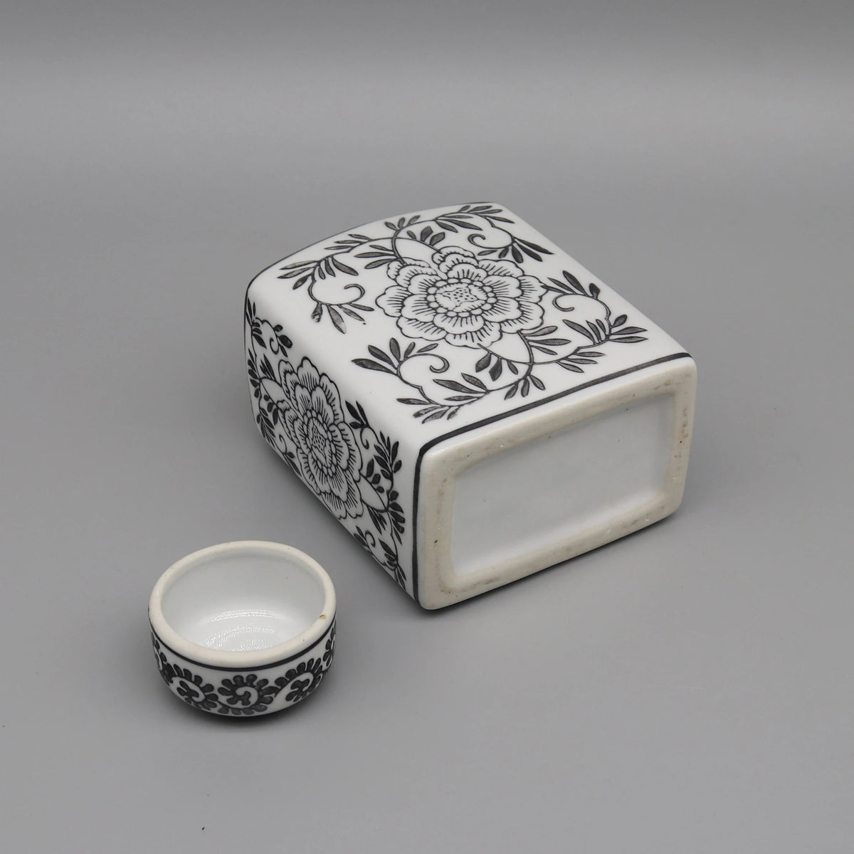 Boîte en céramique blanche et noire avec motif floral détaillé, accompagnée d'une tasse en céramique assortie.