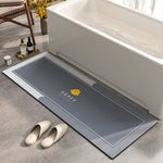 Un tapis de bain antidérapant gris orné d'un logo jaune "Happy" est posé près d'un bain blanc, complétant l'ambiance relaxante de cette salle de bain.