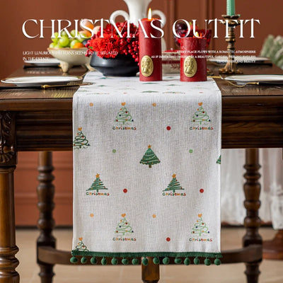 La photo montre une table de fête joliment décorée avec des accessoires de Noël, un chemin de table arborant des motifs d'arbres de Noël qui apporte une touche festive et chaleureuse à l'ensemble.