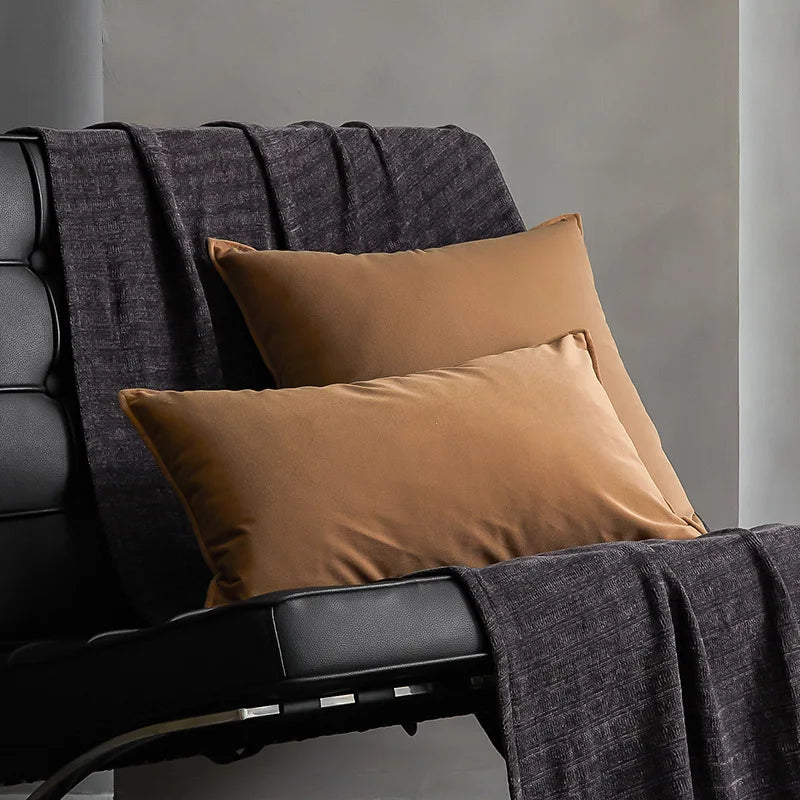 Deux oreillers de couleur beige posés sur un canapé gris foncé. Un plaid gris sombre est également visible sur le canapé.