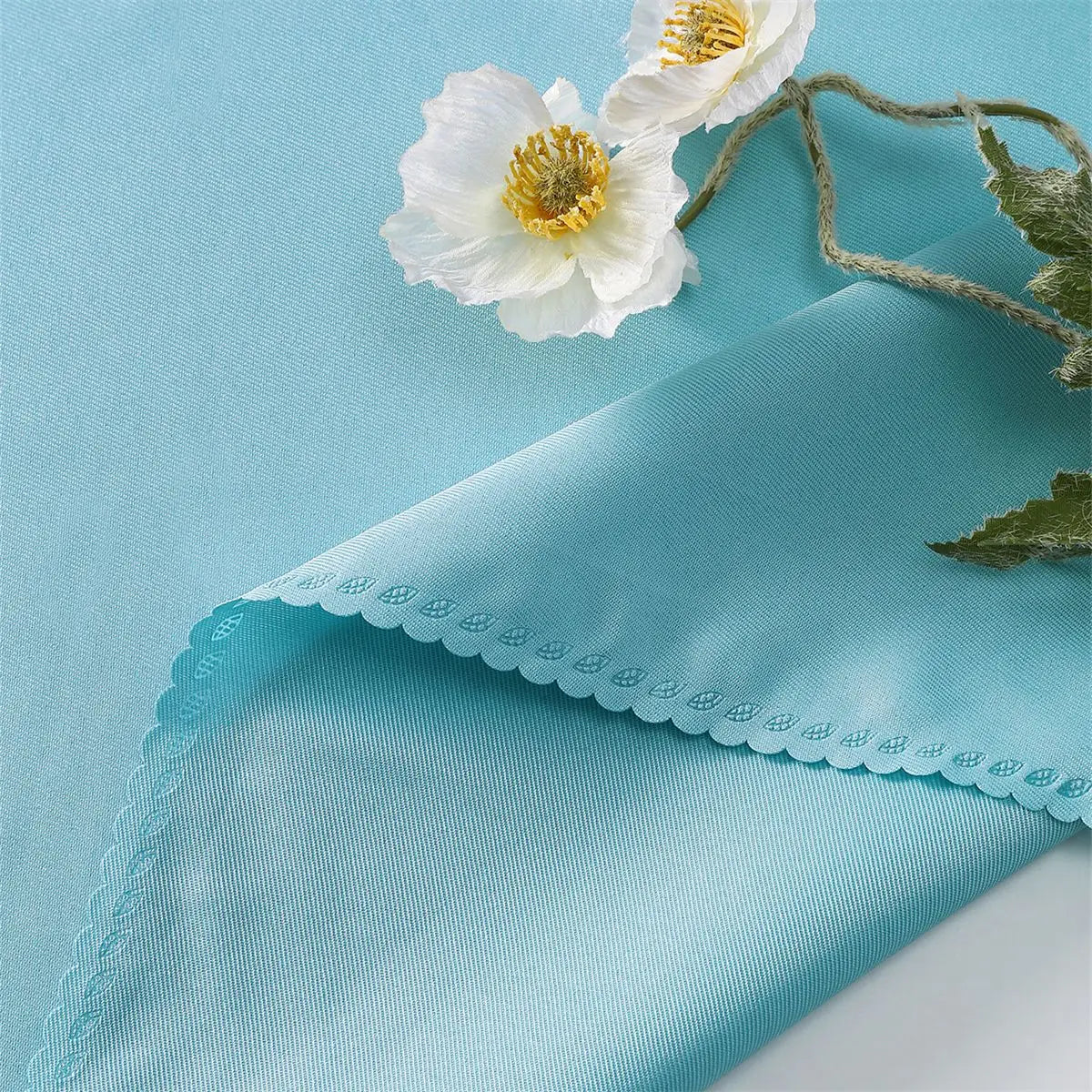 Deux belles fleurs blanches avec des centres jaunes reposent sur un fond bleu clair, avec une texture de tissu piqué délicate.