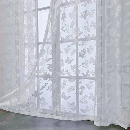 Voilage blanc transparent à motifs papillons et fleurs vu en gros plan dans une pièce lumineuse.
