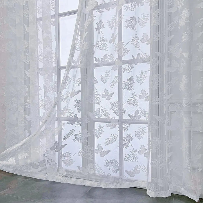 Voilage blanc transparent à motifs papillons et fleurs vu en gros plan dans une pièce lumineuse.