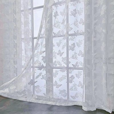 Voilage blanc transparent à motifs papillons et fleurs vu en gros plan dans une pièce lumineuse.