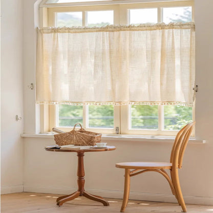 Rideau crème effet lin posé à mi-hauteur d'une grande fenêtre, avec une chaise en bois courbé et une table ronde en bois.
