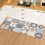 Un tapis de cuisine multicolore, composé de carreaux de motifs géométriques et floraux, décore le sol de cette cuisine moderne équipée de meubles blancs et d'un plan de travail en bois.