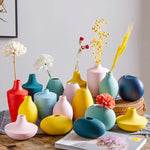 Arrangement de vases colorés et de fleurs séchées sur une surface en bois, créant une décoration d'intérieur chaleureuse et élégante.