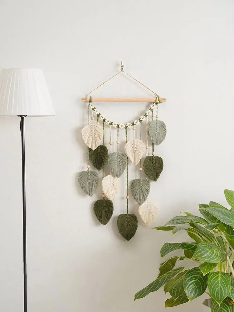 Décoration murale suspendue composée de feuilles macramé vertes et blanches, créant une atmosphère naturelle et apaisante dans la pièce.