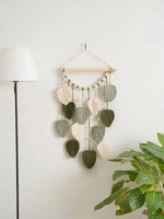 Décoration murale suspendue composée de feuilles macramé vertes et blanches, créant une atmosphère naturelle et apaisante dans la pièce.
