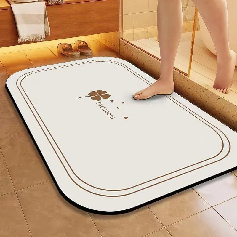 Tapis blanc avec logo trèfle, sur un sol en carrelage dans une salle de bain, avec des pieds de personne visible.