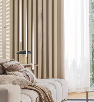Rideau isolant beige dans un salon lumineux avec canapé crème, coussins texturés et lumière naturelle filtrée à travers un voilage blanc.