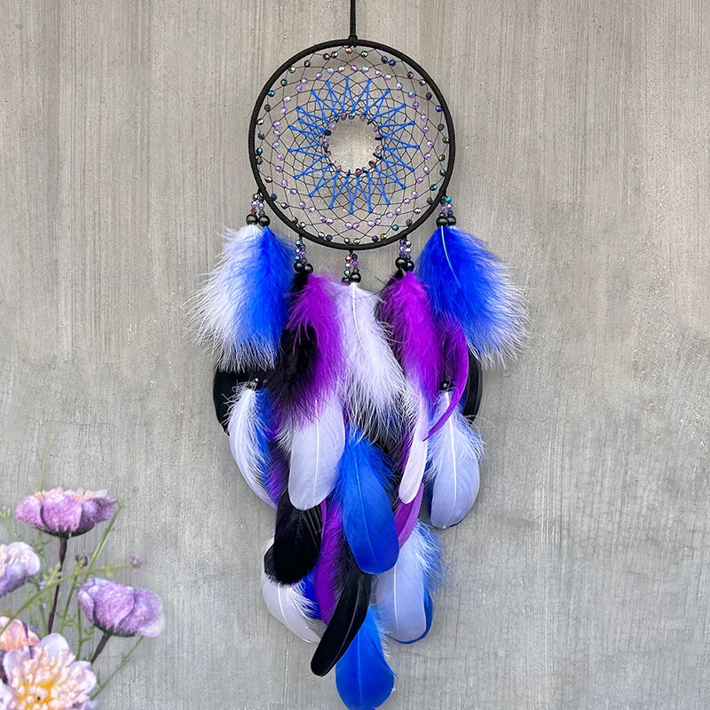 Un attrape-rêves orné de plumes colorées, notamment bleu et violet, suspendu sur un mur gris, avec des fleurs en arrière-plan.