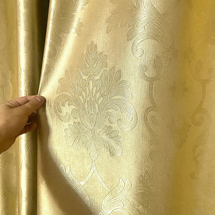 Gros plan sur un rideau doré à motifs baroques avec une main tenant le tissu, mettant en valeur son aspect satiné et sa finesse de tissage.