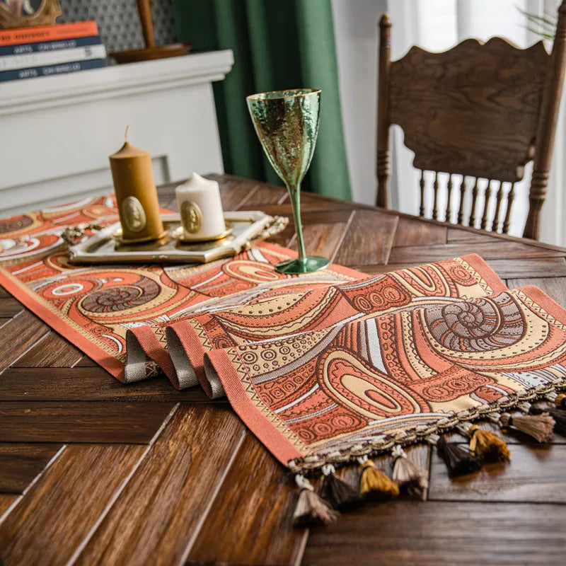 Sur une table en bois se trouve un tapis orné de motifs ethniques colorés, accompagné d'une bougie et d'un verre décoratif, créant une ambiance chaleureuse et intime.