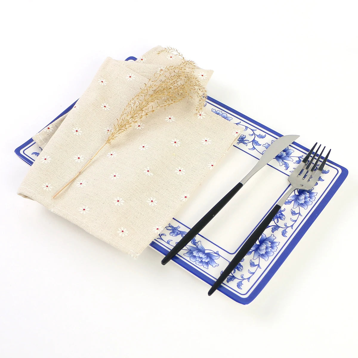 Une assiette et des couverts décorés avec des motifs floraux bleu et blanc, sur un fond blanc avec une serviette de table ornée de fleurs.