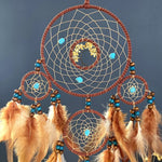 Une superbe attrape-rêves en macramé aux couleurs chaudes et naturelles, composé de motifs géométriques entrelacés et de plumes élégantes qui créent une ambiance apaisante et méditative.