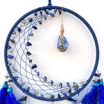 Un cercle décoratif en bleu comprenant une toile recouverte de pierres précieuses et de plumes bleu foncé, avec un pendentif en pierre bleue attaché.