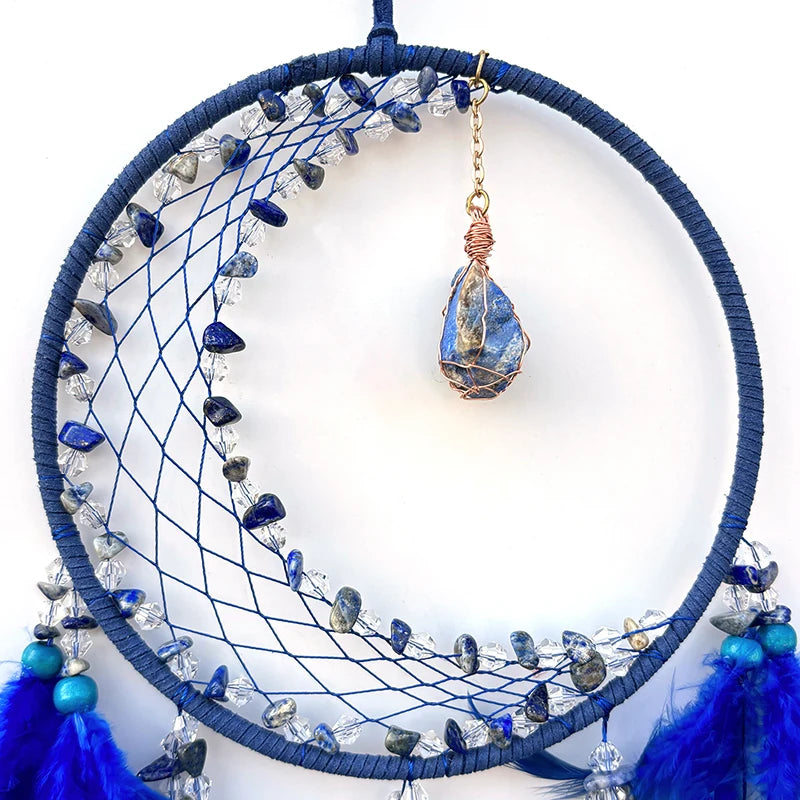 Un cercle décoratif en bleu comprenant une toile recouverte de pierres précieuses et de plumes bleu foncé, avec un pendentif en pierre bleue attaché.