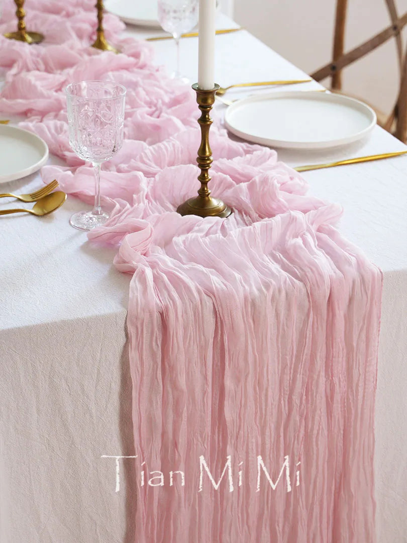 Une table élégante drapée de tissu rose plissé, ornée de bougies allumées, de verres cristallins et d'une assiette blanche, créant une atmosphère sophistiquée et romantique.