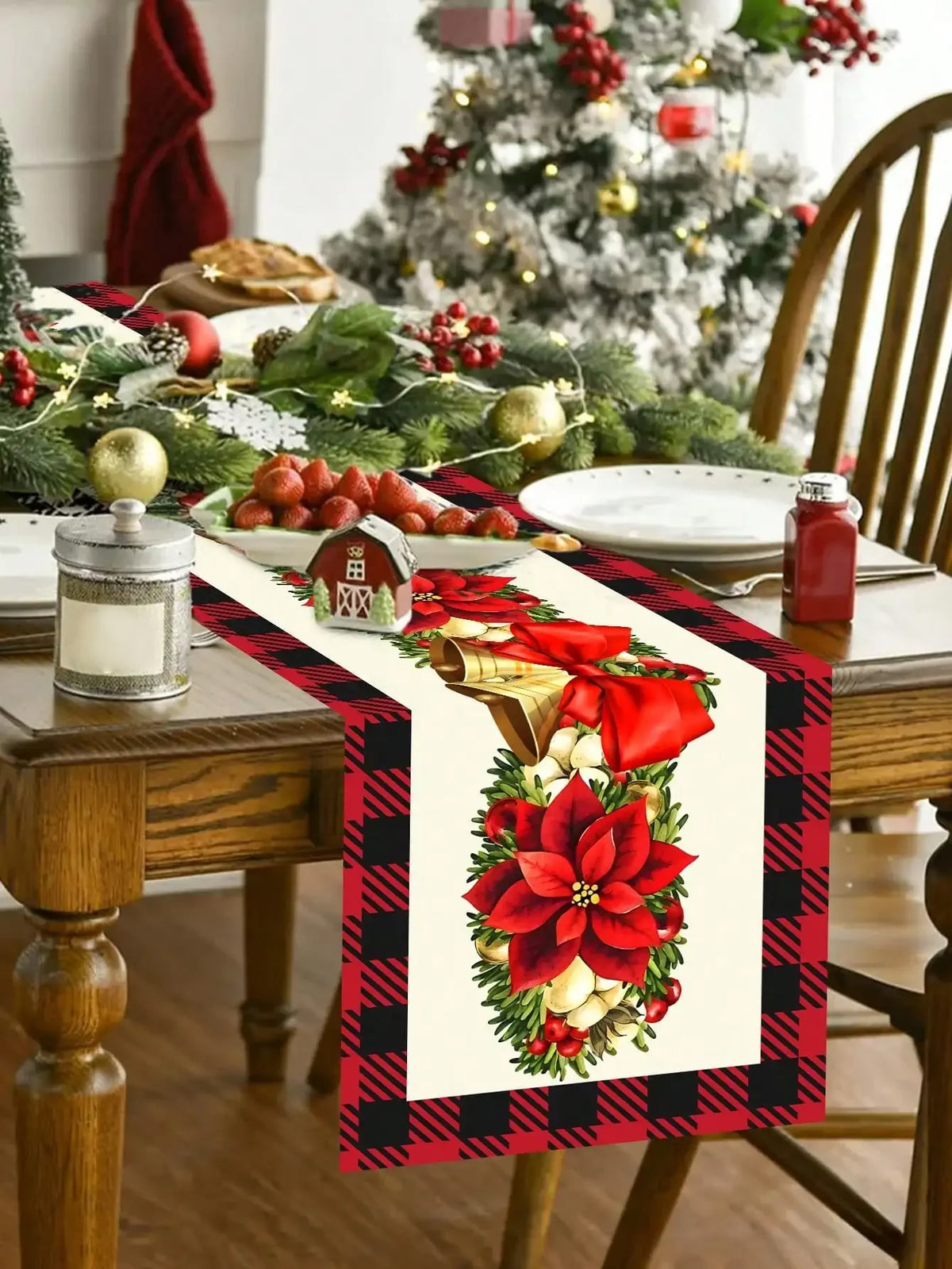 Table de Noël décorée avec un superbe centre de table composé de fleurs rouges, de branches de pin et de baies, sur fond de nappe à motifs écossais rouges et noirs. Un arbre de Noël décoré en arrière-plan complète la scène chaleureuse et festive.