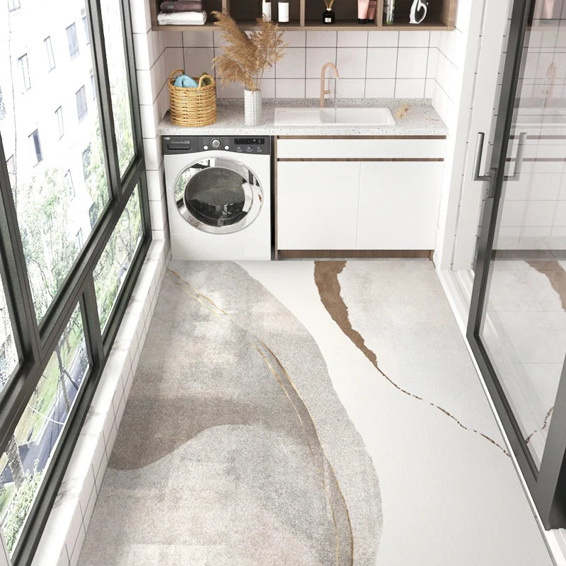 Une cuisine moderne avec lave-linge et armoires blanches sur un plancher en pierre élégant et lumineux, entourée de fenêtres offrant une vue verdoyante.