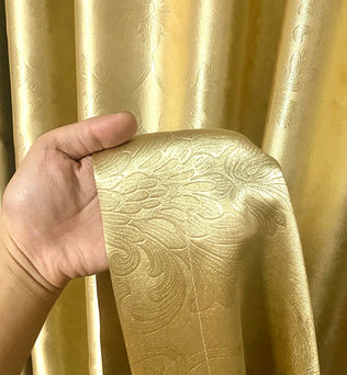 Détail de la texture du rideau doré avec une main tenant un ruban assorti, montrant la qualité et l’épaisseur du tissu.