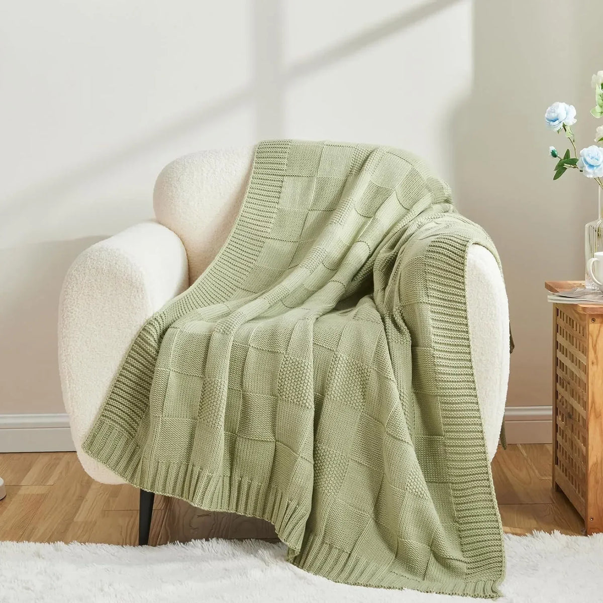 Une belle couverture en tricot vert pâle posée avec soin sur un fauteuil douillet dans un intérieur lumineux et cocooning.