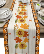 Élégante nappe aux motifs automnaux de tournesols et de feuilles colorées, posée sur une table en bois avec des assiettes et des couverts.