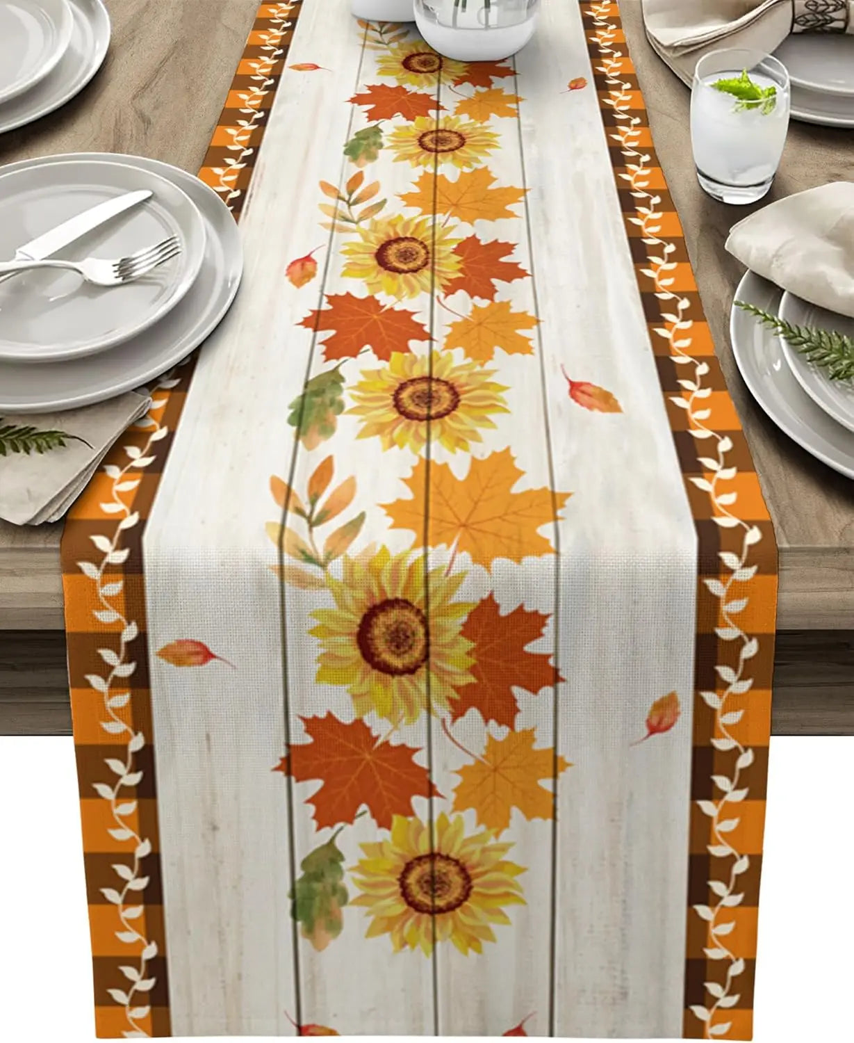 Élégante nappe aux motifs automnaux de tournesols et de feuilles colorées, posée sur une table en bois avec des assiettes et des couverts.