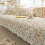 Sur un canapé douillet, une literie fleurie et texturée, avec des coussins assortis, crée une ambiance chaleureuse et apaisante dans cette pièce ensoleillée.