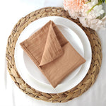 Une belle serviette de table beige en gros plan, posée sur un dessous de plat en fibre tressée, entouré de fleurs roses épanouies.